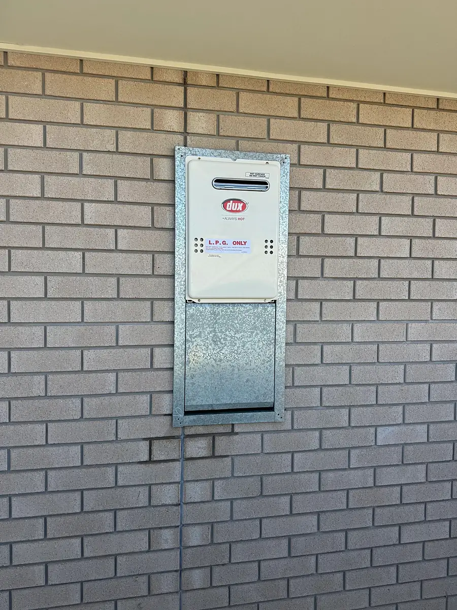LPG continuous-flow hot water unit set into a brick wall with a pipe cover