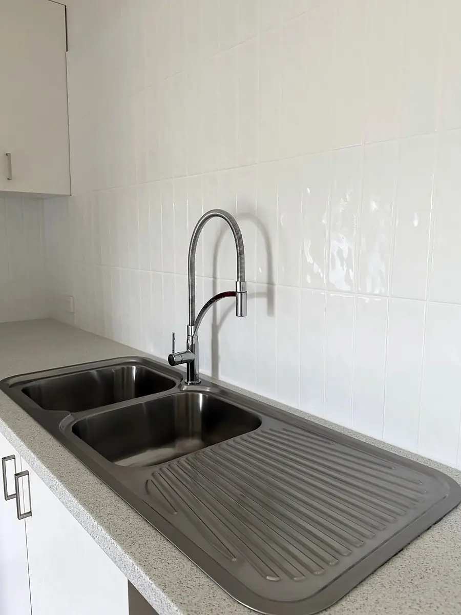Double bowl stainless sink and pull-down mixer installed in a new white kitchen