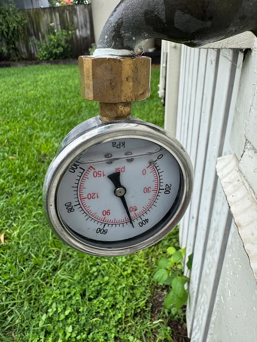 Water pressure gauge fitted to a garden tap beside a fence