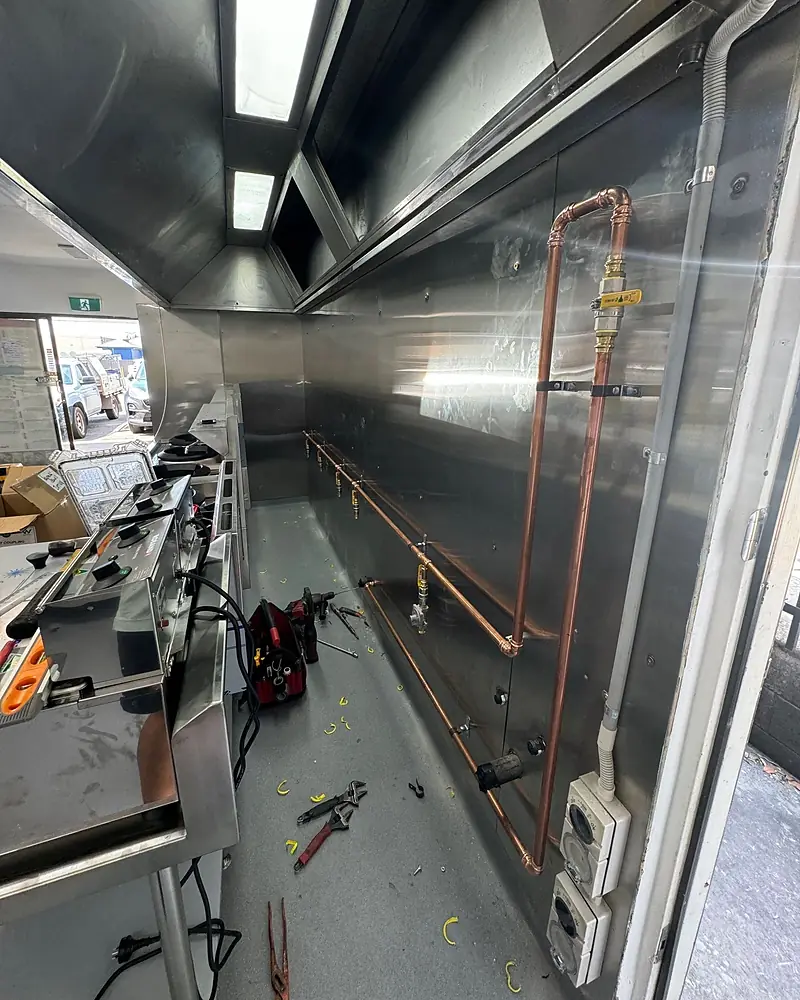 New copper gas pipework with yellow-handled isolation valves run along a stainless steel commercial kitchen wall
