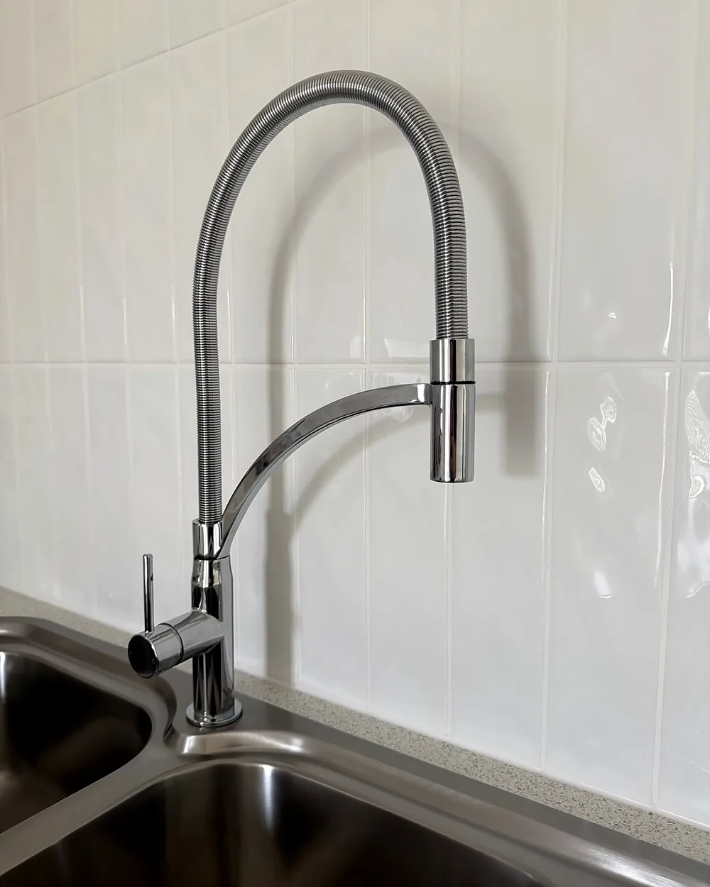 New chrome pull-down kitchen mixer over a stainless sink with white tiles